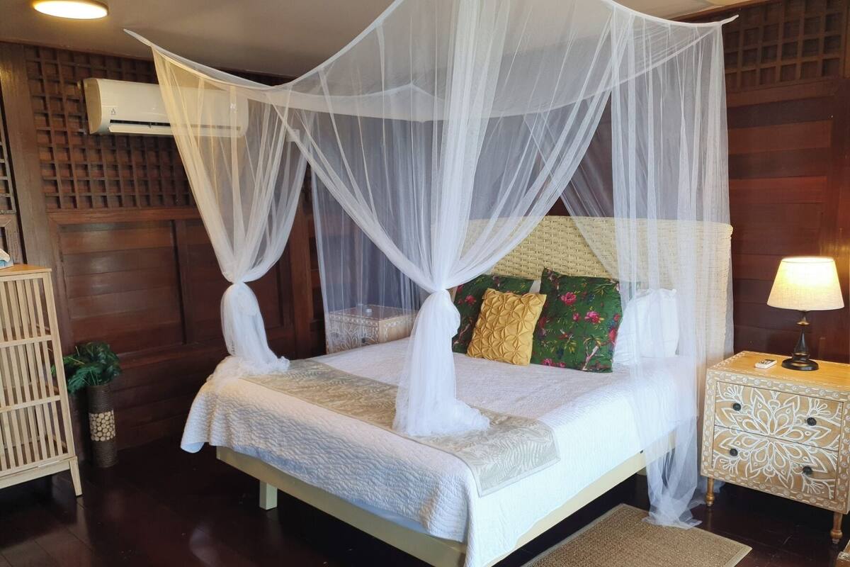 A neatly arranged bedroom with a four-poster bed, a bedside table with a lamp, and a small potted plant.