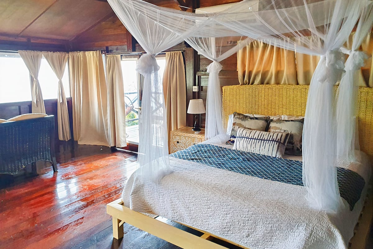 A bed with a canopy, a wicker headboard, and a view of the outdoors.