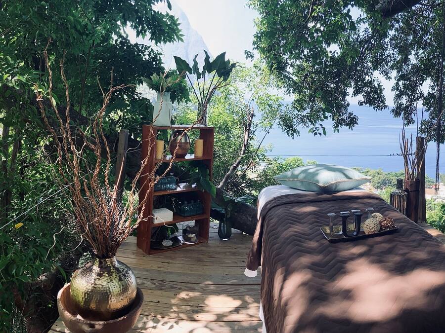 Una terraza de madera con una cama, un estante con objetos y vista al mar.