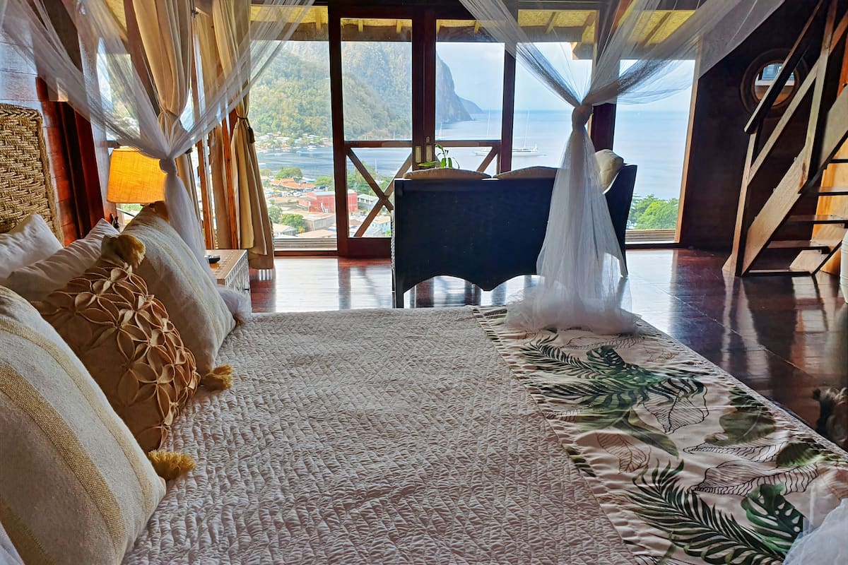 A bedroom with a large bed, a view of the sea, and a wooden floor.