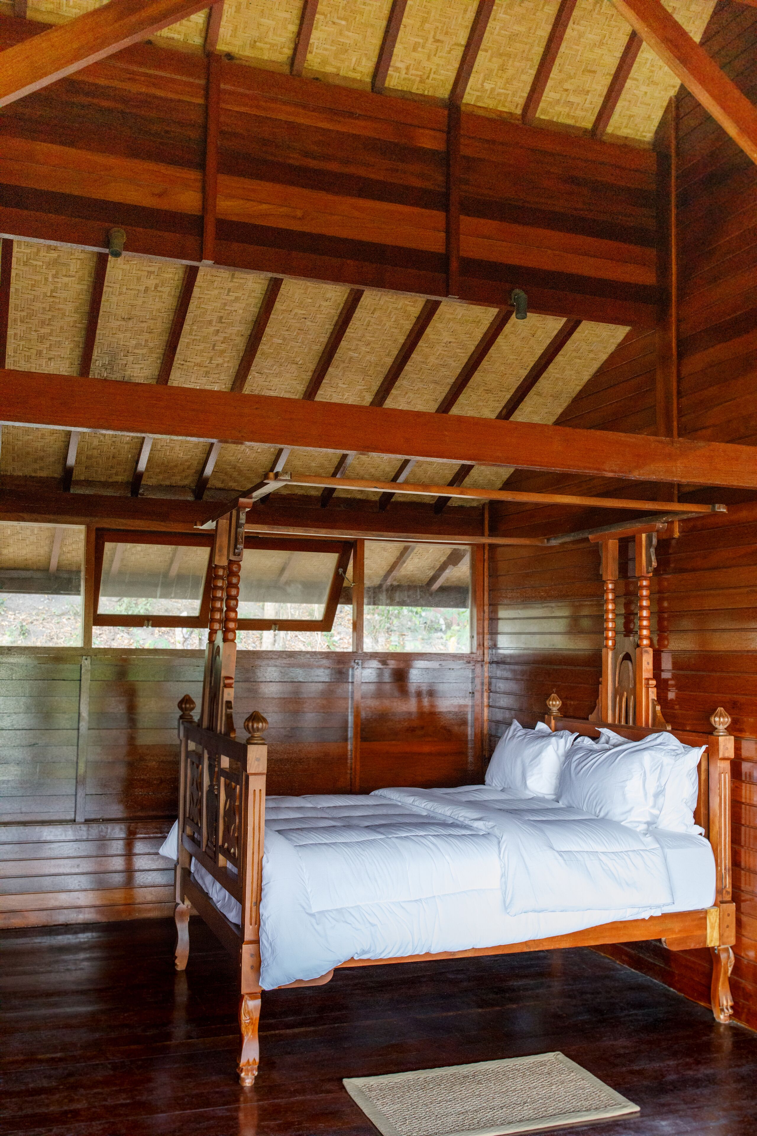 Un lit à baldaquin en bois, avec une literie blanche, dans une chambre de style chalet, dotée d’un toit de chaume et de murs en bois.