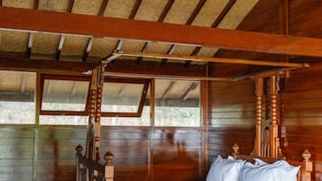 Un lit à baldaquin en bois, avec une literie blanche, dans une chambre de style chalet, dotée d’un toit de chaume et de murs en bois.