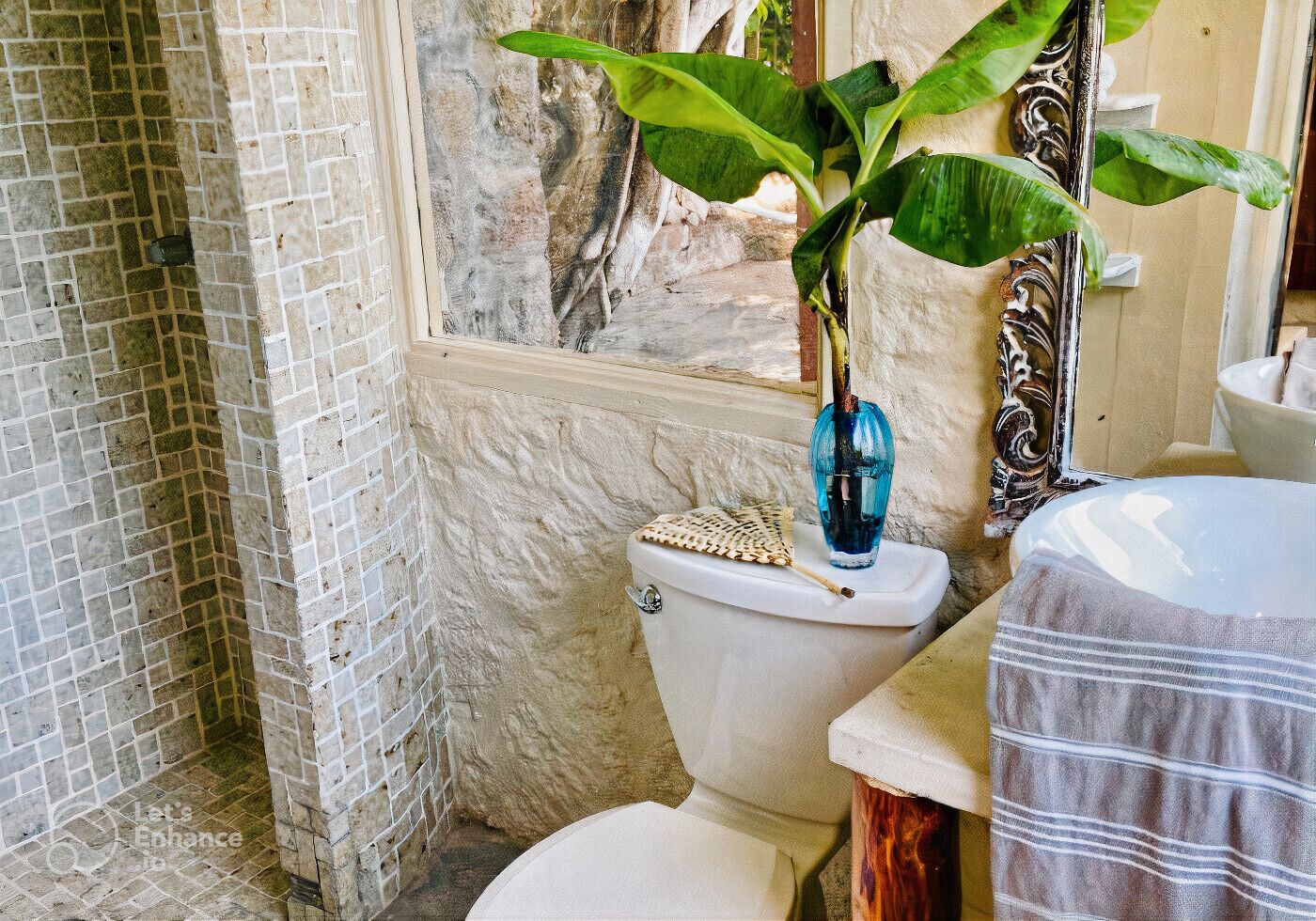 Un baño con ducha azulejada, inodoro con un jarrón azul y una planta.