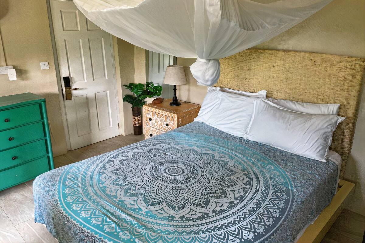 A bedroom with a bed, a green dresser, a nightstand with a lamp, and a door.