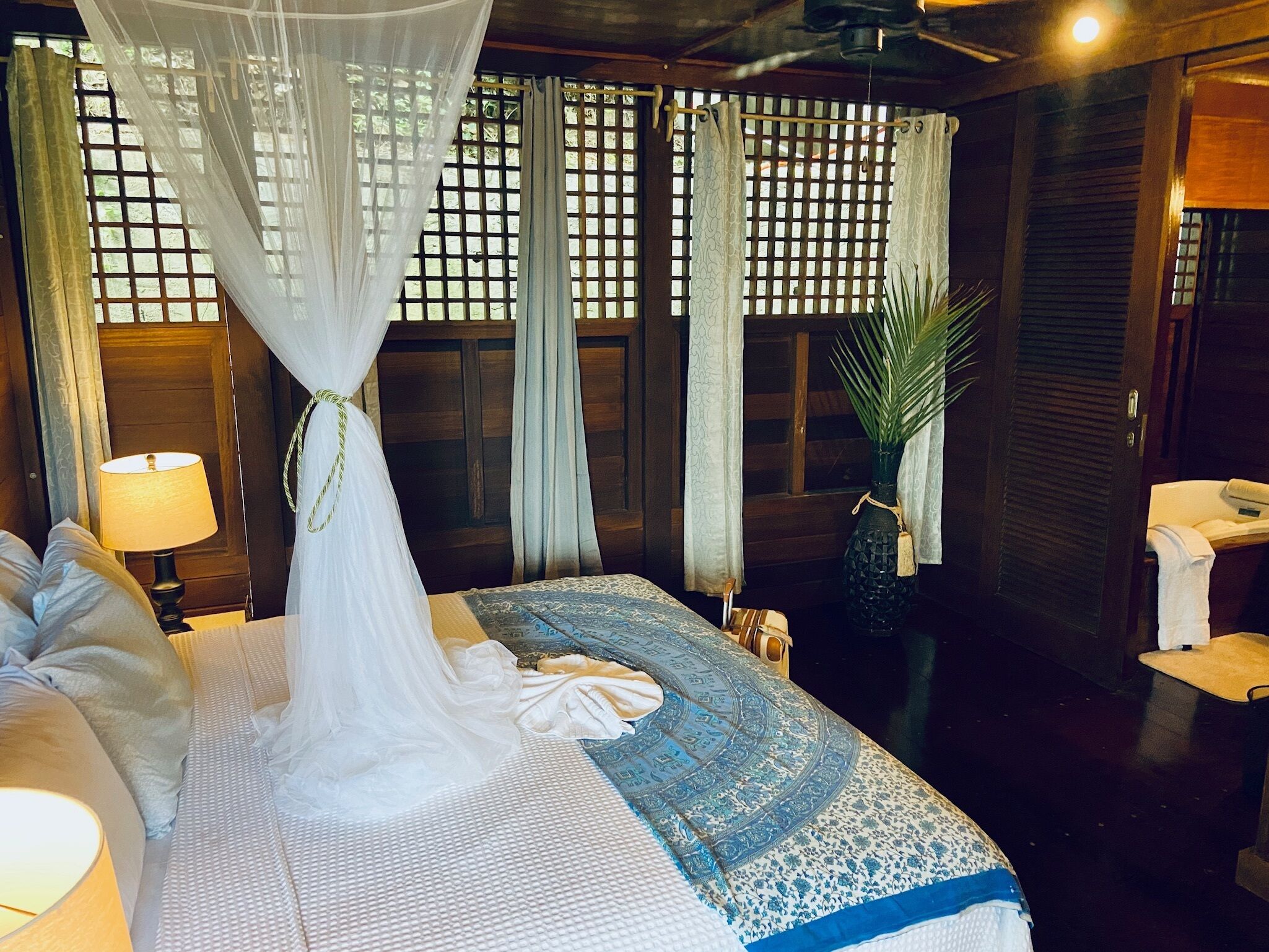 A neatly made bed with a canopy, a bedside lamp, and a potted plant.