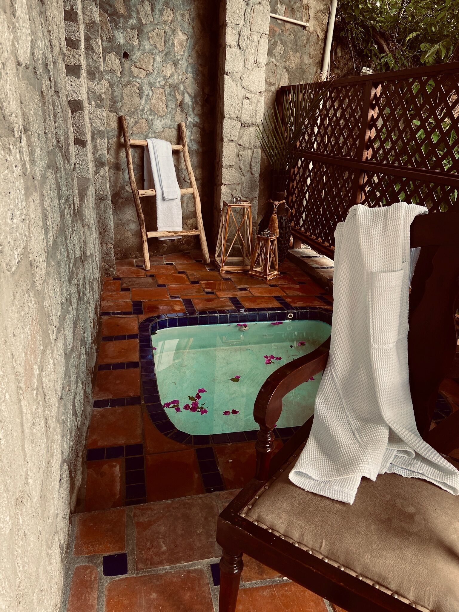 A stone-walled bathroom with a bathtub, wooden ladder, and a wooden chair.