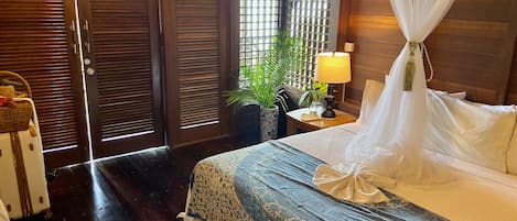 A bedroom with a bed, a nightstand, a lamp, a potted plant, and a suitcase.
