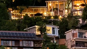 Zona residencial en una ladera con varias casas, algunas con paneles solares, rodeada de vegetación densa.