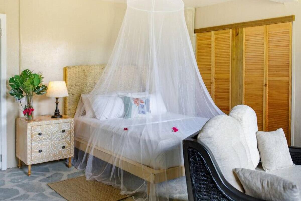 A neatly arranged bedroom with a canopy bed, a bedside table with a lamp, a chair, and a wardrobe.