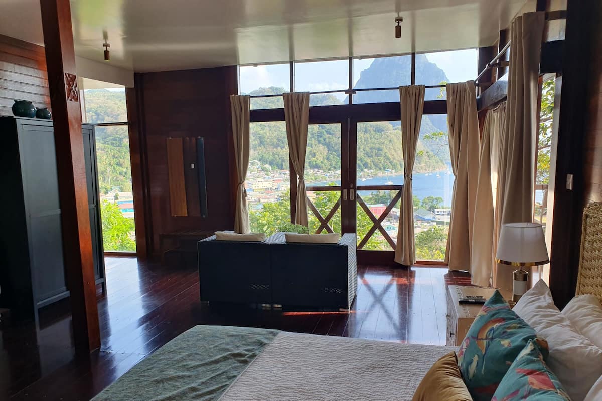 A spacious room with a large bed, a sofa, and a view of a mountainous landscape through large windows.