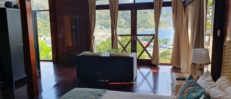 Una habitación amplia con una cama grande, un sofá y vistas a un paisaje montañoso a través de ventanas grandes.