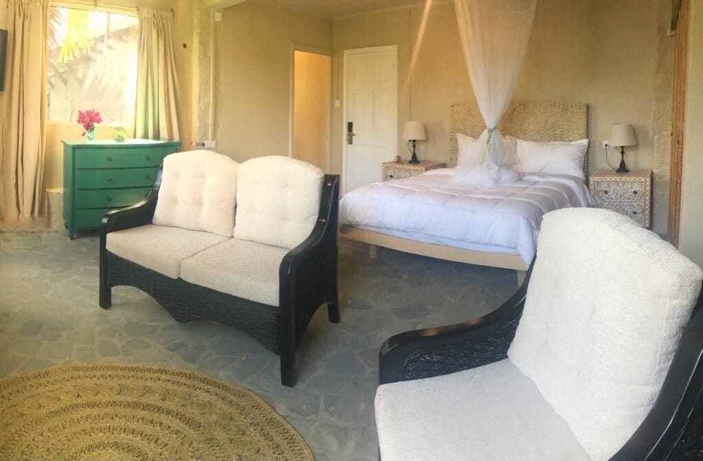 Ein Schlafzimmer mit einem Bett, zwei Stühlen, einem Nachttisch, einer Kommode und einem Fenster mit Vorhängen.