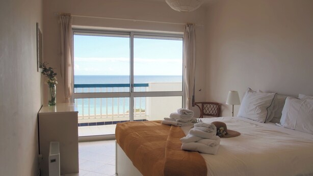 A hotel room with a bed, a desk, a lamp, a chair, and a view of the ocean. - 2 bedroom apartment 30 meters from beach, stunning views Praia da Rocha PORTIMAO (Portimão)