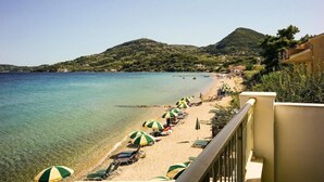 Une plage à l’eau claire, avec des parasols verts et une montagne en arrière-plan.