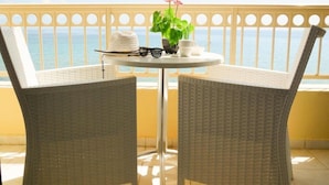 Un balcon avec une table ronde, deux chaises en osier, un chapeau, des lunettes de soleil, une plante en pot et une tasse.