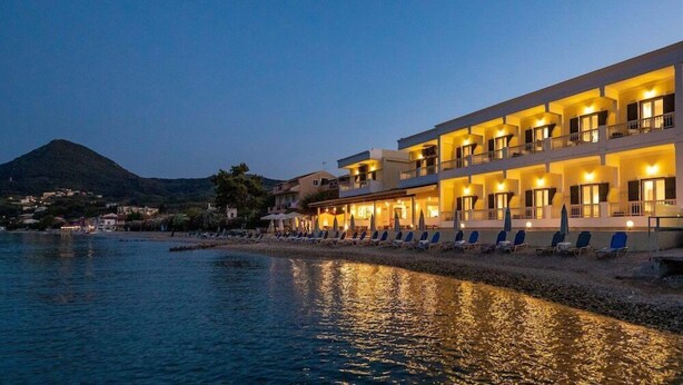 Un hôtel doté de nombreux balcons donnant sur une plage, d’un espace piscine avec des chaises longues et d’une montagne en arrière-plan.