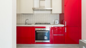 Een keuken met rode kastjes, een roestvrijstalen afzuigkap, een ingebouwde oven en een gasfornuis.
