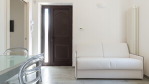 Een moderne woonkamer met een glazen eettafel, een witte bank en een bruine deur.
