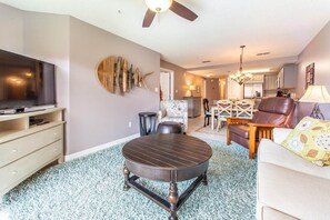 A living room with a round coffee table, a television, and a dining area with a chandelier.
