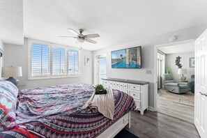Une chambre à coucher avec un lit, un ventilateur de plafond, un tableau et une vue sur l’extérieur.