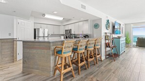 A modern kitchen with bar stools, a large island, and a view to the outside.
