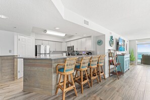 Une cuisine moderne avec des tabourets de bar, un grand îlot central et une vue sur l’extérieur.