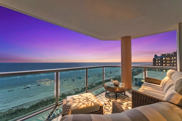 Un balcon avec vue sur la plage et l’océan au coucher du soleil.