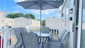 A covered outdoor patio with a table and chairs, surrounded by a white railing. - Excellent Caravan 4 Birth Sleeps 6 Tranquil Site (Colchester)