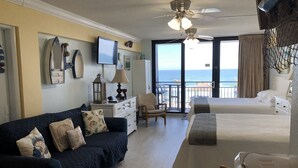Ein Hotelzimmer mit Balkon, Bett, Sofa, Schreibtisch und Fernseher.