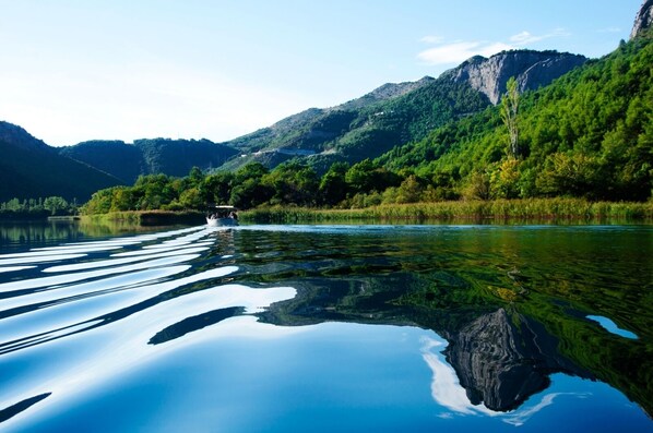 Een kalm meer met heldere reflecties, omgeven door weelderige groene heuvels en een boot in de verte.