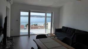Een moderne woonkamer met een grote schuifpui die uitkomt op een balkon met uitzicht op zee.