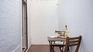 A small outdoor patio with a wooden table and chairs, a bottle of wine, and an open book. - FLH Vila Rosário Cosy Flat II (Lisbon)