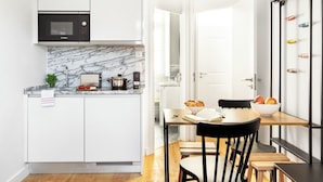 A modern kitchen with white cabinetry, a Bosch microwave, marble backsplash, and a dining area with a wooden table and chairs. - FLH Vila Rosário Cosy Flat II (Lisbon)
