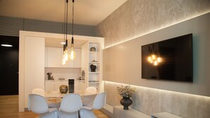 A modern living room with a dining area, a flat-screen TV mounted on the wall, and a built-in bench.