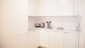 A modern kitchen with white cabinetry, a toaster, a kettle, and a coffee maker on the countertop.