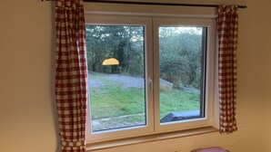 Una habitación con un ventanal grande, cortinas a cuadros, un banco con cojines y vistas a un jardín.