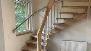 Una escalera de madera con barandillas metálicas, un radiador y una ventana con vistas a árboles.