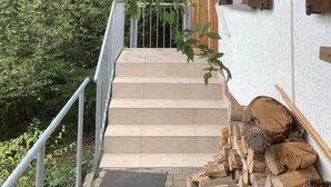 Una escalera de madera que conduce a una casa de exterior blanco y contraventanas marrones, rodeada de follaje.