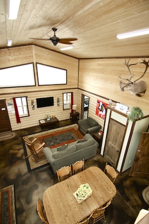 A log cabin interior with a dining table, chairs, a sofa, a television, and a ceiling fan.