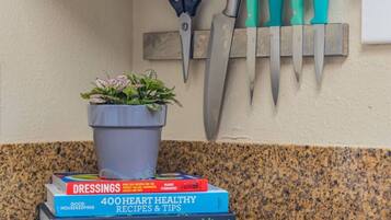 A kitchen counter with a potted plant, a set of knives, and three cookbooks.