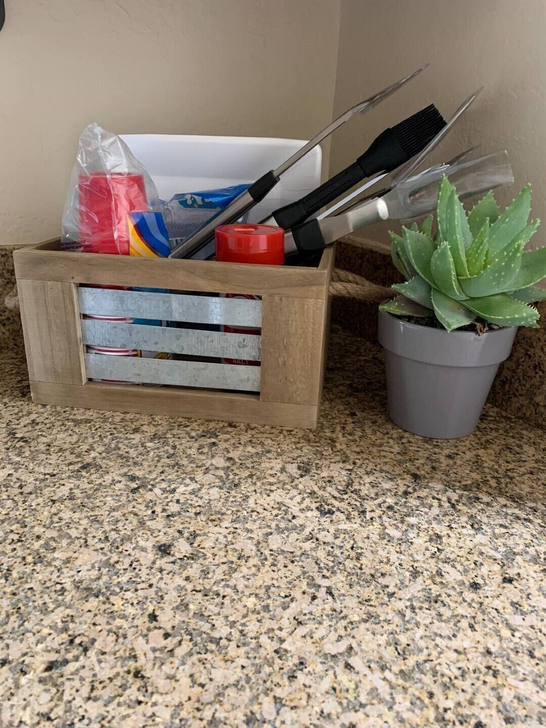 A wooden crate with tools and a potted succulent on a granite countertop.