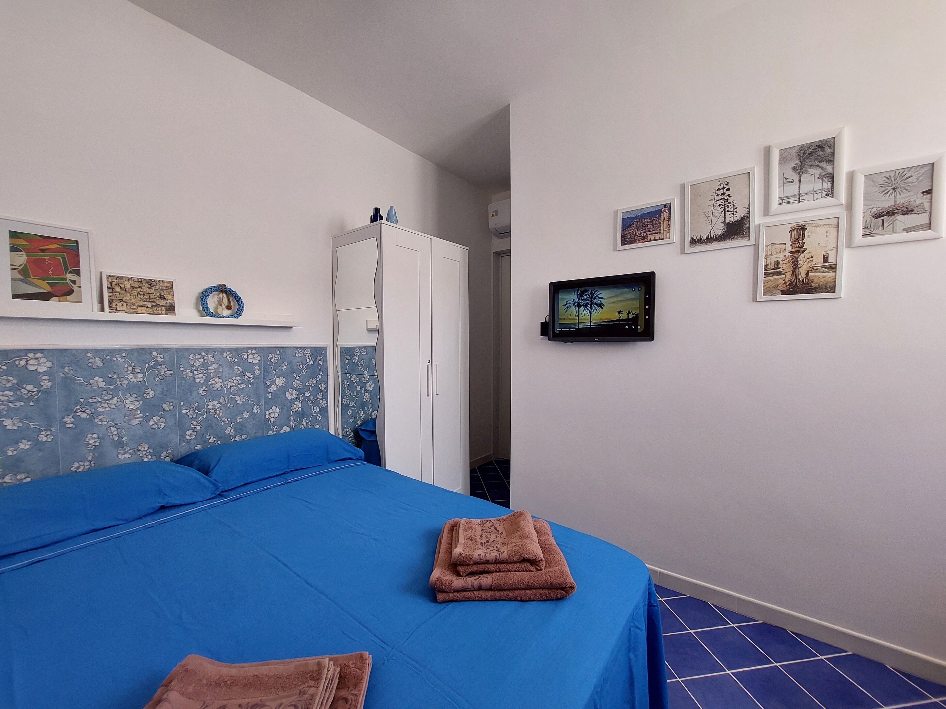 Een slaapkamer met een blauwe spreidekbed, een witte garderobe en een wandgemonteerde flatscreen televisie.