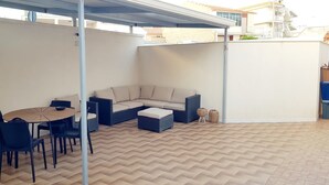 A covered patio area with a round table and chairs, a sofa, and a small ottoman. - AB_Apartment  (Marina di Ragusa)
