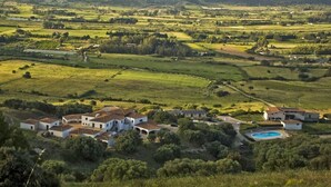 A rural landscape with a cluster of white buildings, a swimming pool, and surrounding fields.