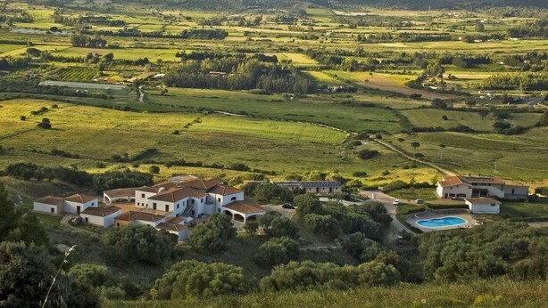 Un paysage rural avec un ensemble de bâtiments blancs, une piscine et des champs environnants.
