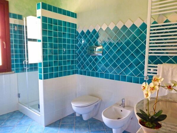 A bathroom with a shower, toilet, bidet, and a potted orchid.