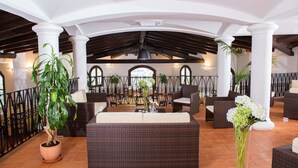 A spacious indoor patio with wicker furniture, potted plants, and a view of the city through arched windows.