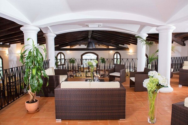 A spacious indoor patio with wicker furniture, potted plants, and a view of the city through arched windows. - Tenuta Su Vrau (Torpe)