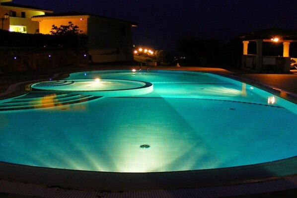 Piscina nocturna con bordes iluminados y un desagüe central.