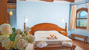 A bedroom with a wooden bed, bedside tables, a bench, a window with curtains, and a view of the outdoors.